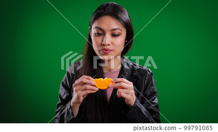 Young woman bites into an orange slice 99791085
