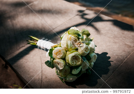 A pair of gold wedding rings on a bride's bouquet with white flowers A pair of gold wedding rings on a bride's bouquet with white flowers 99791972