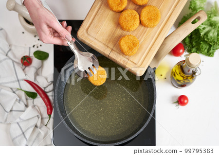 Woman puts cheese balls into frying pan with hot cooking oil 99795383