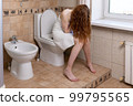 A young girl sits on the toilet at home in the toilet and cries because of abdominal pain or pregnancy. 99795565