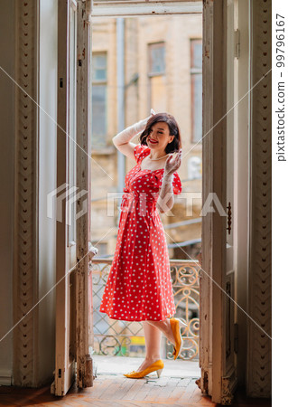 a beautiful and happy brunette women in red retro dress in the balcony doorway  99796167