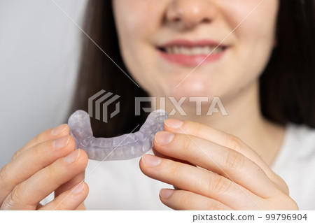 A woman holds dental mouthguard, splint for the treatment of dysfunction of the temporomandibular joints, bruxism, malocclusion, to relax the muscles of the jaw. 99796904
