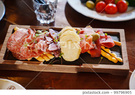 a wooden tray with snacks made of dried meat, sausage, cheese and potato chips. a wooden tray with snacks made of dried meat, sausage, cheese and potato chips. 99796905