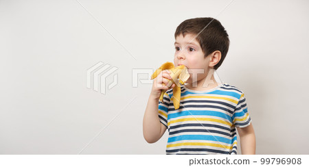 A 4-year-old boy eats a banana. Long banner with space for text on a white background. Fruits and vitamins for preschool children A 4-year-old boy eats a banana. Long banner with space for text on a white background. Fruits and vitamins for preschool children 99796908