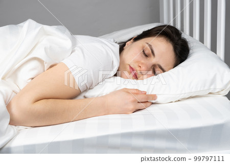 A 30-year-old brunette woman sleeps in bed on her stomach on a pillow made of artificial fluff. Sleeping on your stomach. 99797111
