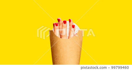 Female fingers instead of fries into packaging against yellow studio background. Surrealism and creativity. Food pop art photography. Female fingers instead of fries into packaging against yellow studio background. Surrealism and creativity. Food pop art photography. 99799460