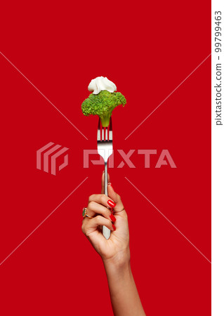 Food pop art photography. Female hand holding broccoli on fork against red studio background. Healthy eating. Food pop art photography. Female hand holding broccoli on fork against red studio background. Healthy eating. 99799463