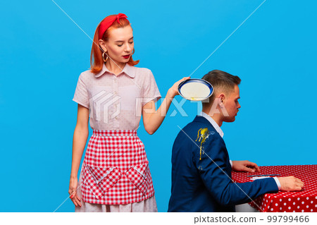 Young red head woman dropping breakfast with fried eggs at males costume. Models against blue studio background. Food pop art photography. 99799466