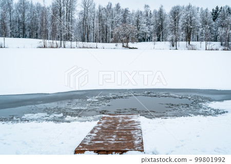 Snow-covered wooden path descending into the cold water 99801992