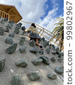 Back view of a girl climbing a playground equipment with stones 99802967