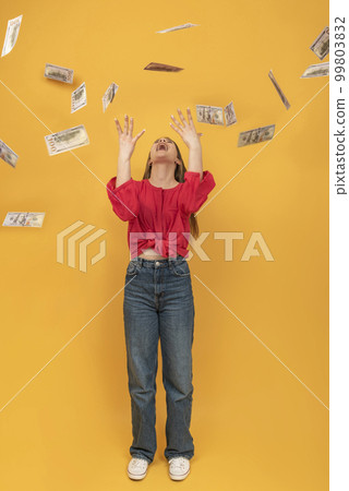 Young laughing woman tossing up dollar bills while standing against orange background. Vertical frame. 99803832