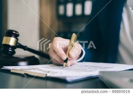 Close up view of auction hammer on the desk in lawyer office and lawyer writing document as courtroom. Close up view of auction hammer on the desk in lawyer office and lawyer writing document as courtroom. 99805019