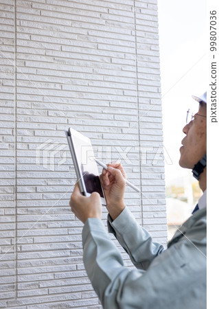 A male worker inspecting the outer wall of the veranda of a detached house A male worker inspecting the outer wall of the veranda of a detached house 99807036