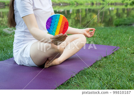 A woman meditates in nature and eats a reusable bubble wrap pop it antistress toy. Deal with stress at work with Pop it, yoga and meditation. A woman meditates in nature and eats a reusable bubble wrap pop it antistress toy. Deal with stress at work with Pop it, yoga and meditation. 99810187