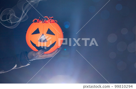 A bucket of candy in the form of a pumpkin lantern Jack on a black background in a hand. Halloween banner place for text. A bucket of candy in the form of a pumpkin lantern Jack on a black background in a hand. Halloween banner place for text. 99810294