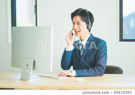 A young man in a suit wearing a headset and doing inside sales 99810565