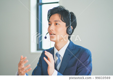 A young man in a suit wearing a headset and doing inside sales A young man in a suit wearing a headset and doing inside sales 99810569