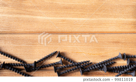 Self-cutters on a wood brown background banner with space for text. Construction tools, self-tapping screws for fastening. Black screw hardware. Self-cutters on a wood brown background banner with space for text. Construction tools, self-tapping screws for fastening. Black screw hardware. 99811019