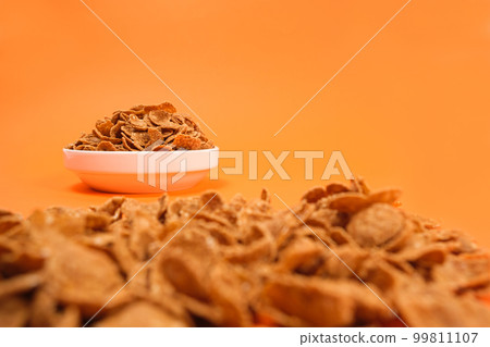 Close-up of wheat flakes on orange background, quick cereal healthy breakfasts. Close-up of wheat flakes on orange background, quick cereal healthy breakfasts. 99811107