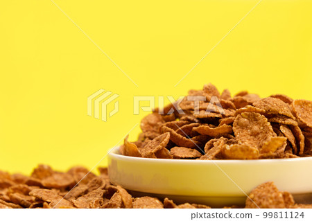 Durum wheat flakes - quick breakfast cereal on a plate on a yellow background, space for text. Durum wheat flakes - quick breakfast cereal on a plate on a yellow background, space for text. 99811124
