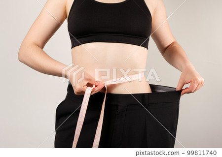 A woman in large pants measures the circumference of the abdomen, the concept of losing weight and a healthy lifestyle A woman in large pants measures the circumference of the abdomen, the concept of losing weight and a healthy lifestyle 99811740