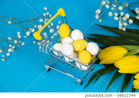 Easter white and yellow quail painted eggs in a shopping cart on a blue background. Easter Sale and shopping Easter white and yellow quail painted eggs in a shopping cart on a blue background. Easter Sale and shopping 99811744