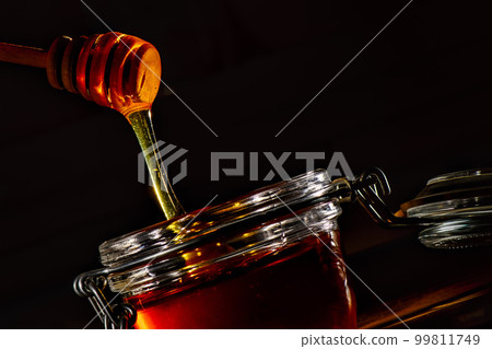 Glass jar with honey and the natural wooden stick Glass jar with honey and the natural wooden stick 99811749