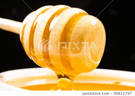 Liquid natural bee honey in a white ceramic bowl with a wooden spoon. Liquid natural bee honey in a white ceramic bowl with a wooden spoon. 99811787