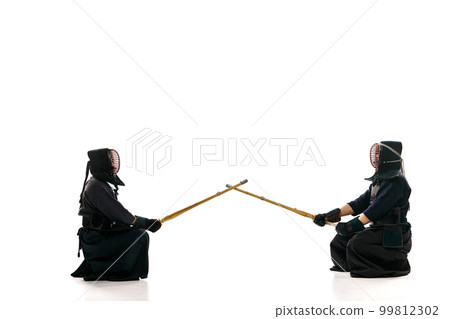 Start of fight. Two men, professional kendo athletes in uniform with helmet with bamboo shinai sword against white studio background Start of fight. Two men, professional kendo athletes in uniform with helmet with bamboo shinai sword against white studio background 99812302
