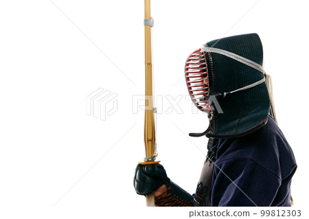 Side view. Portrait of man, professional kendo athlete in uniform posing with shinai sword against white studio background Side view. Portrait of man, professional kendo athlete in uniform posing with shinai sword against white studio background 99812303