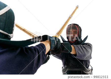 Close-up image of two men, professional kendo athletes in uniform training bamboo shinai sword against white studio background Close-up image of two men, professional kendo athletes in uniform training bamboo shinai sword against white studio background 99812311