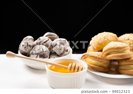 Liquid natural bee honey in a white ceramic bowl with a wooden spoon, with honey cookies and cocoa cookies. Liquid natural bee honey in a white ceramic bowl with a wooden spoon, with honey cookies and cocoa cookies. 99812323