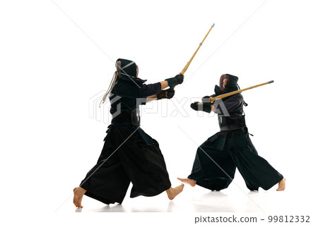 Two men, professional kendo athletes in motions, fighting, training with bamboo shinai sword against white studio background Two men, professional kendo athletes in motions, fighting, training with bamboo shinai sword against white studio background 99812332