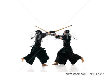 Fighters. Two men, professional kendo athletes in uniform with helmet training with bamboo shinai sword against white studio background 99812344