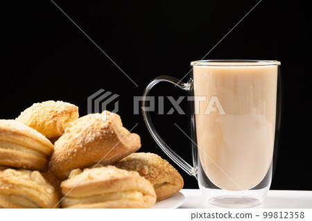Tea with milk in a glass cup with a double bottom and cakes on a black background Tea with milk in a glass cup with a double bottom and cakes on a black background 99812358