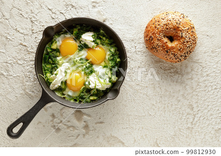 Green shakshuka with frshly baked bagel. Fried eggs in a cast iron pan. Traditional meal of the Jewish cuisine Green shakshuka with frshly baked bagel. Fried eggs in a cast iron pan. Traditional meal of the Jewish cuisine 99812930