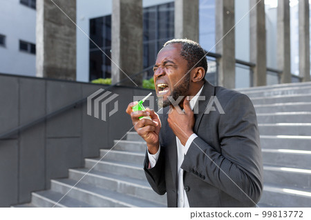 An older African American man in a suit clears his throat from pain and inflammation while standing outside an office center. An older African American man in a suit clears his throat from pain and inflammation while standing outside an office center. 99813772