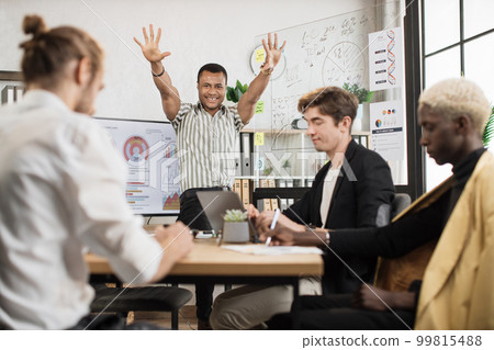 African man standing near big monitor and glass flip chart with raised hands celebrating success 99815488