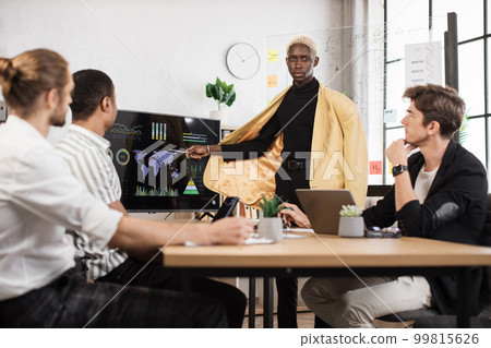 Group of four partners sitting at desk and listening speech of african american man near monitor 99815626