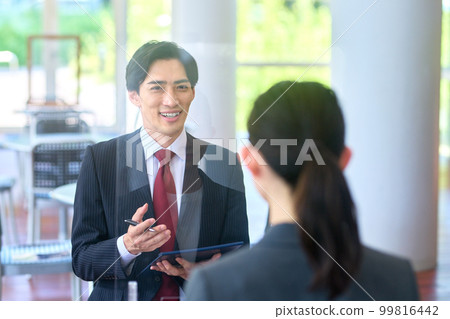 一位穿著西裝的商人在辦公室大廳用亞克力板面試 一位穿著西裝的商人在辦公室大廳用亞克力板面試 99816442