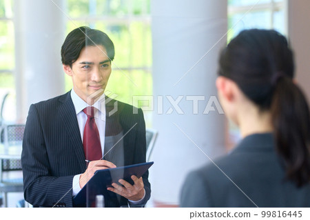 A businessman in a suit interviewing in an office lobby with an acrylic board 99816445