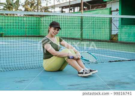 smiling asian female tennis player sitting relaxed holding racket 99816741