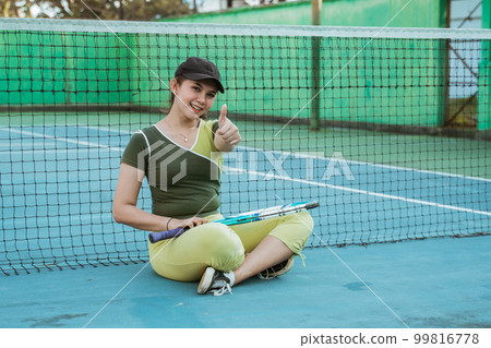 beautiful tennis player sitting with thumbs up on tennis court 99816778