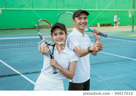 smiling mixed doubles tennis player with thumbs up holding racket smiling mixed doubles tennis player with thumbs up holding racket 99817018