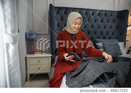 asian woman in veil folding clothes and preparing suitcase asian woman in veil folding clothes and preparing suitcase 99817205