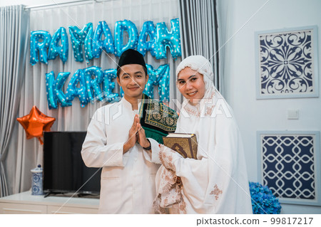 Muslim couple standing with greeting gesture and holding the Quran 99817217
