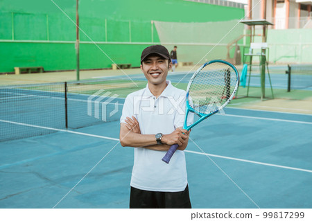 Smiling male athlete with crossed hands holding a racket 99817299