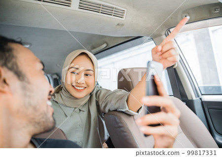 Asian woman passenger in hijab with pointing finger tells driver Asian woman passenger in hijab with pointing finger tells driver 99817331