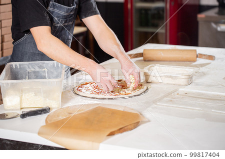 Cooking pizza. arranges cheese ingredients on the dough preform. Closeup hand of chef baker in uniform white apron cook at kitchen 99817404