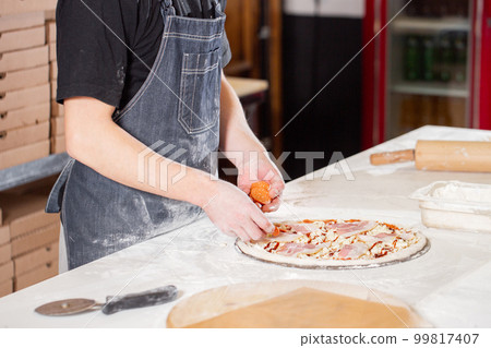 Cooking pizza. arranges cheese ingredients on the dough preform. Closeup hand of chef baker in uniform white apron cook at kitchen 99817407